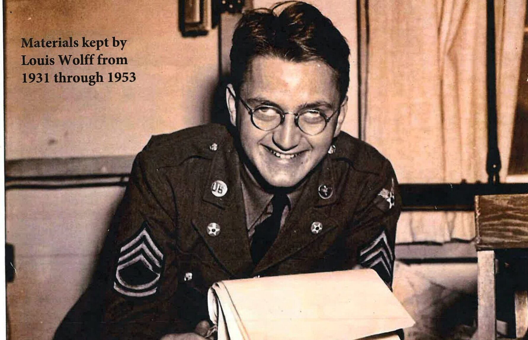 A smiling soldier in uniform reads a letter indoors.