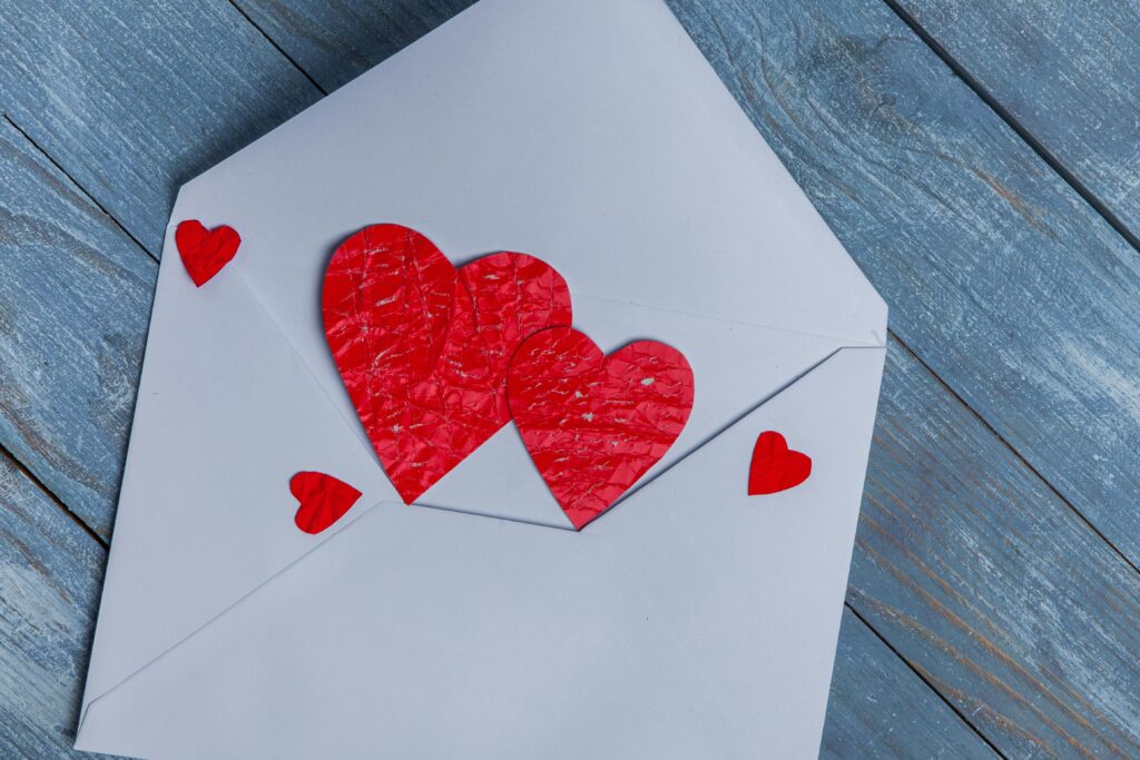 Red paper hearts on a white envelope on wooden surface.
