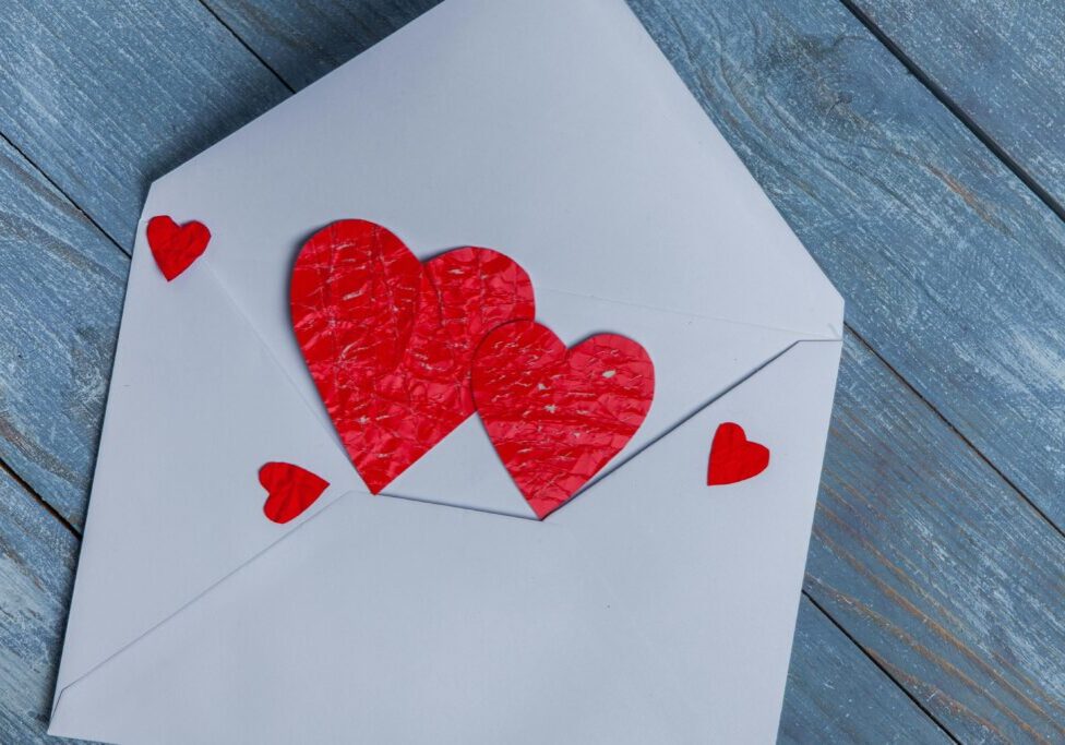 Red paper hearts on a white envelope on wooden surface.